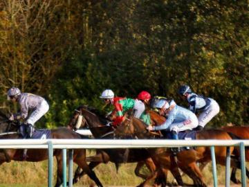 Jockeys mounted on Racehorses gallop around the track at Southwell Racecourse.