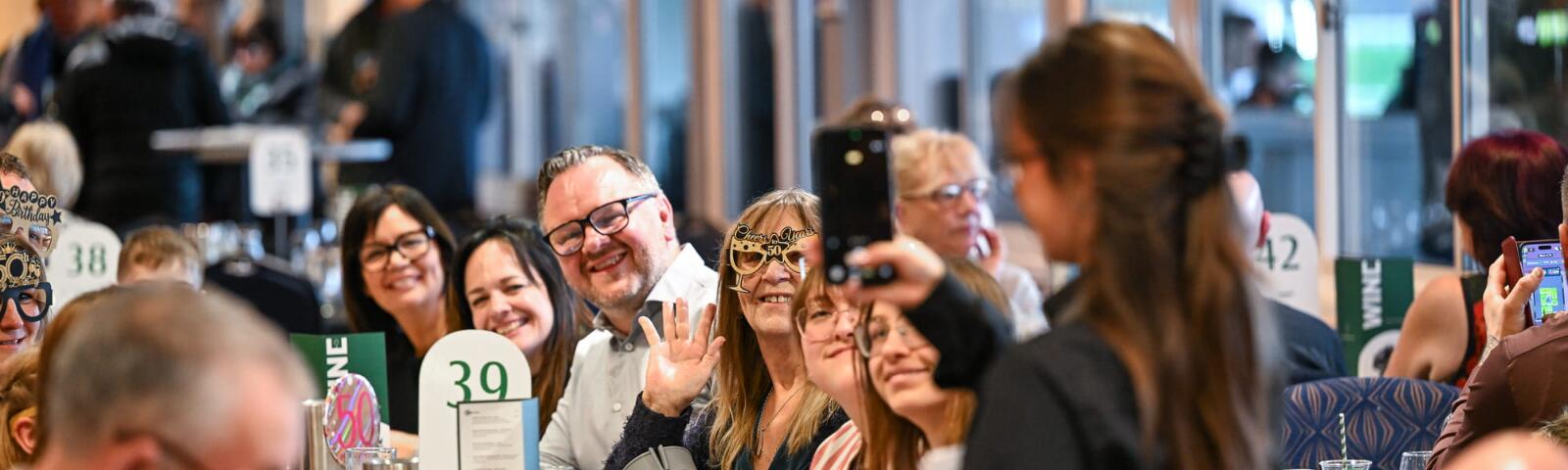 Group of smiling people having their photo taken while sitting at a table.