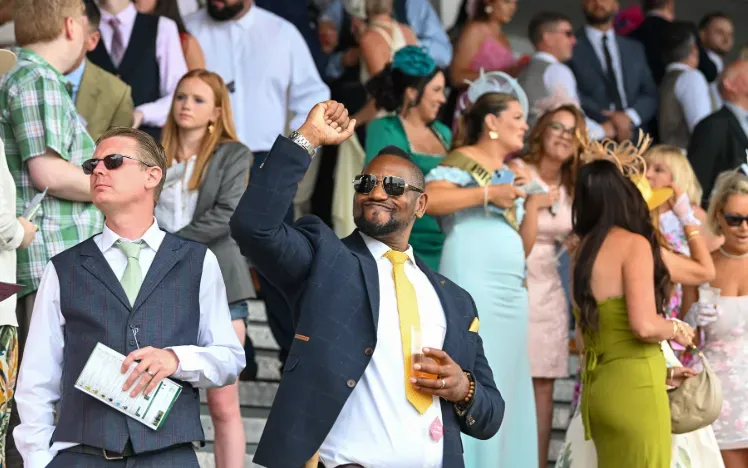 A well dressed man in a suit punches the air in celebration in the grandstand at Southwell