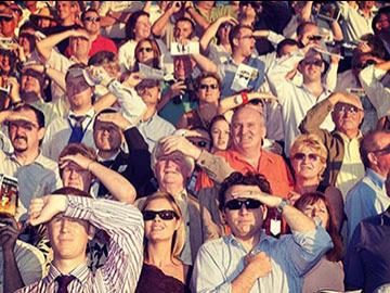 Crowds shielding their eyes from the sun as they watch racing at Southwell Racecourse