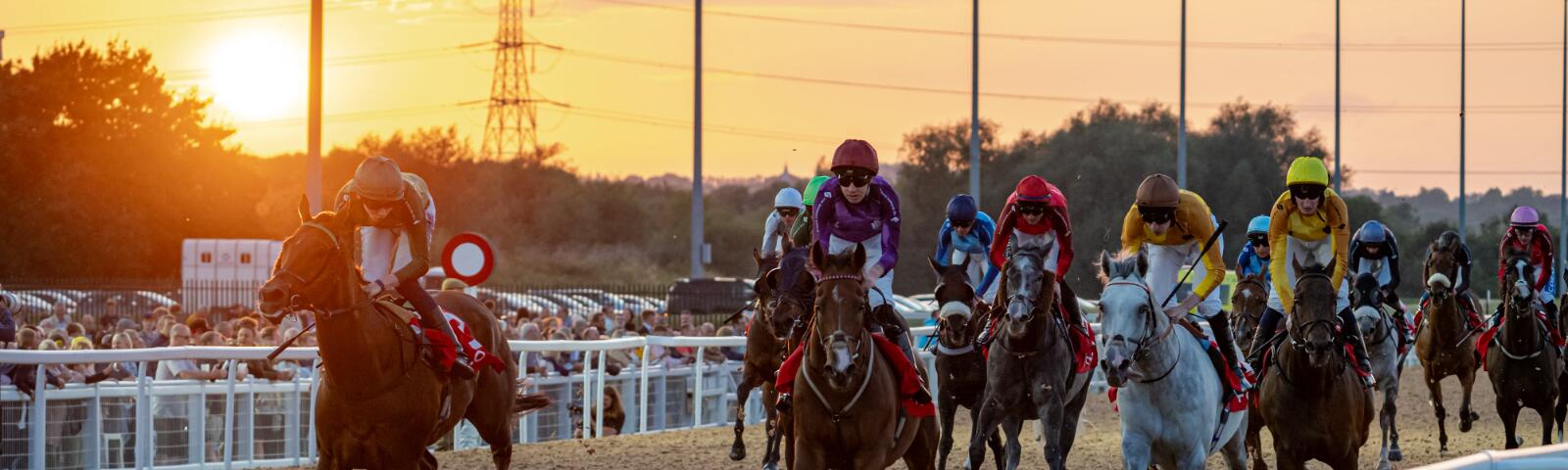 Horses and jockeys race at Southwell during sunset