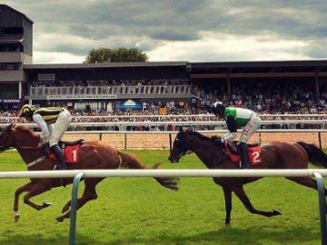 Two horses almost neck and neck running around the track at Southwell Racecourse.